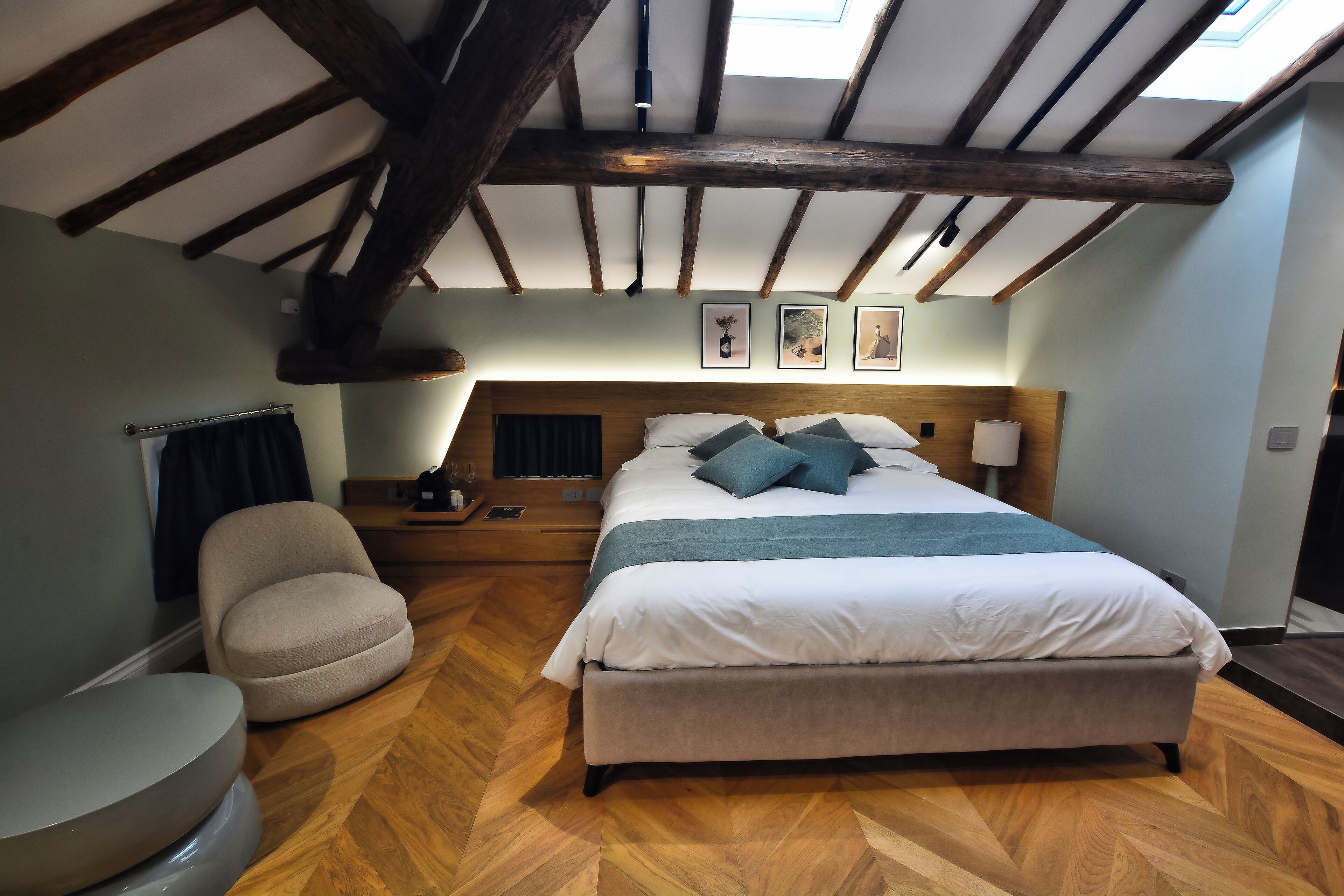 Quarto com cama grande, cadeira, mesa de cabeceira e piso de madeira.