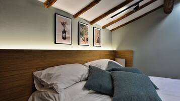 Un dormitorio con cabecera de madera, cama con ropa de cama blanca y gris, y tres cuadros enmarcados en la pared.