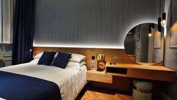 Moderni hotellihuone, jossa on suuri sänky, puinen yöpöytä, peili ja seinään kiinnitetty valaisin.