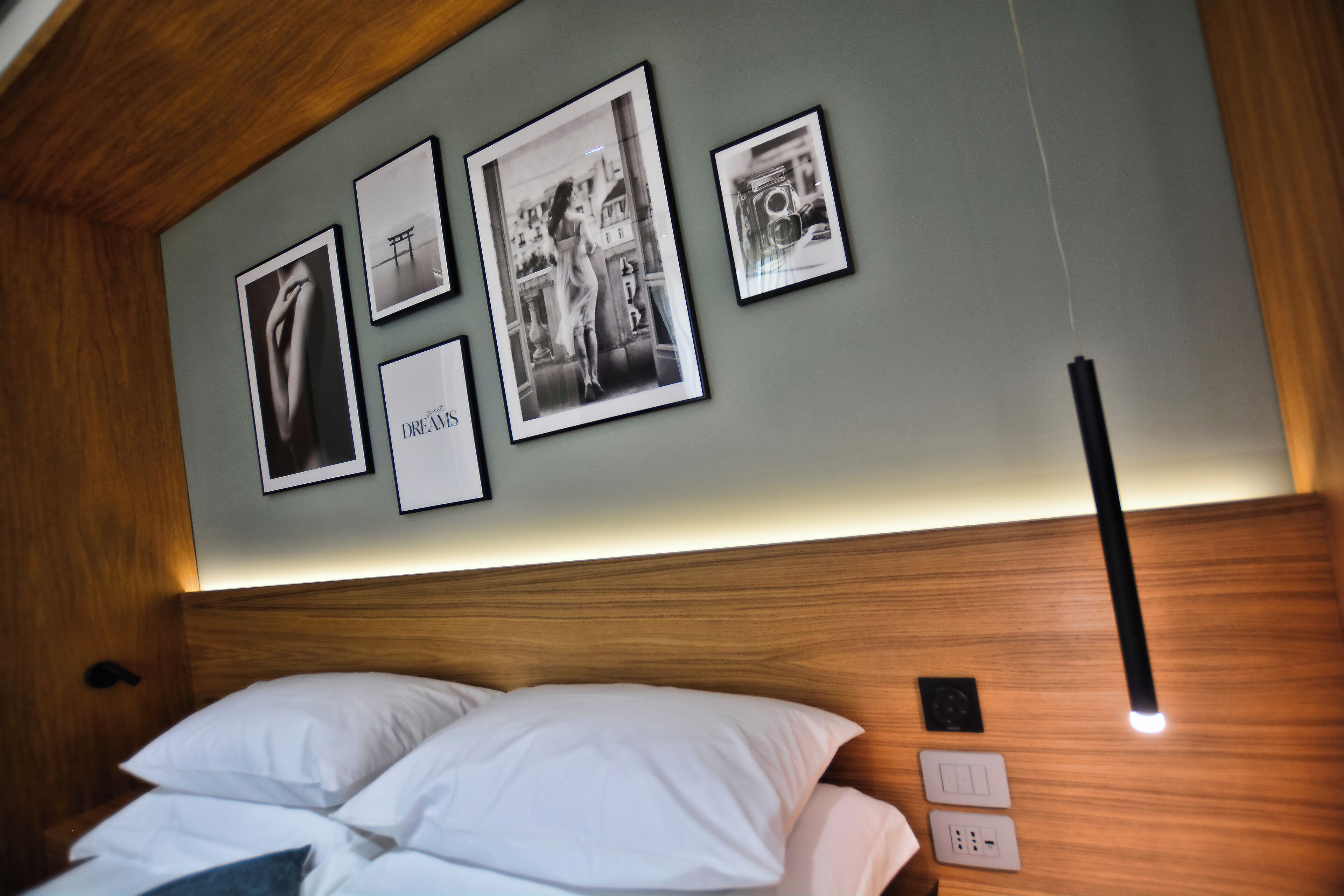 A hotel room with a wooden headboard, a bed with white linens, and a wall with framed pictures.