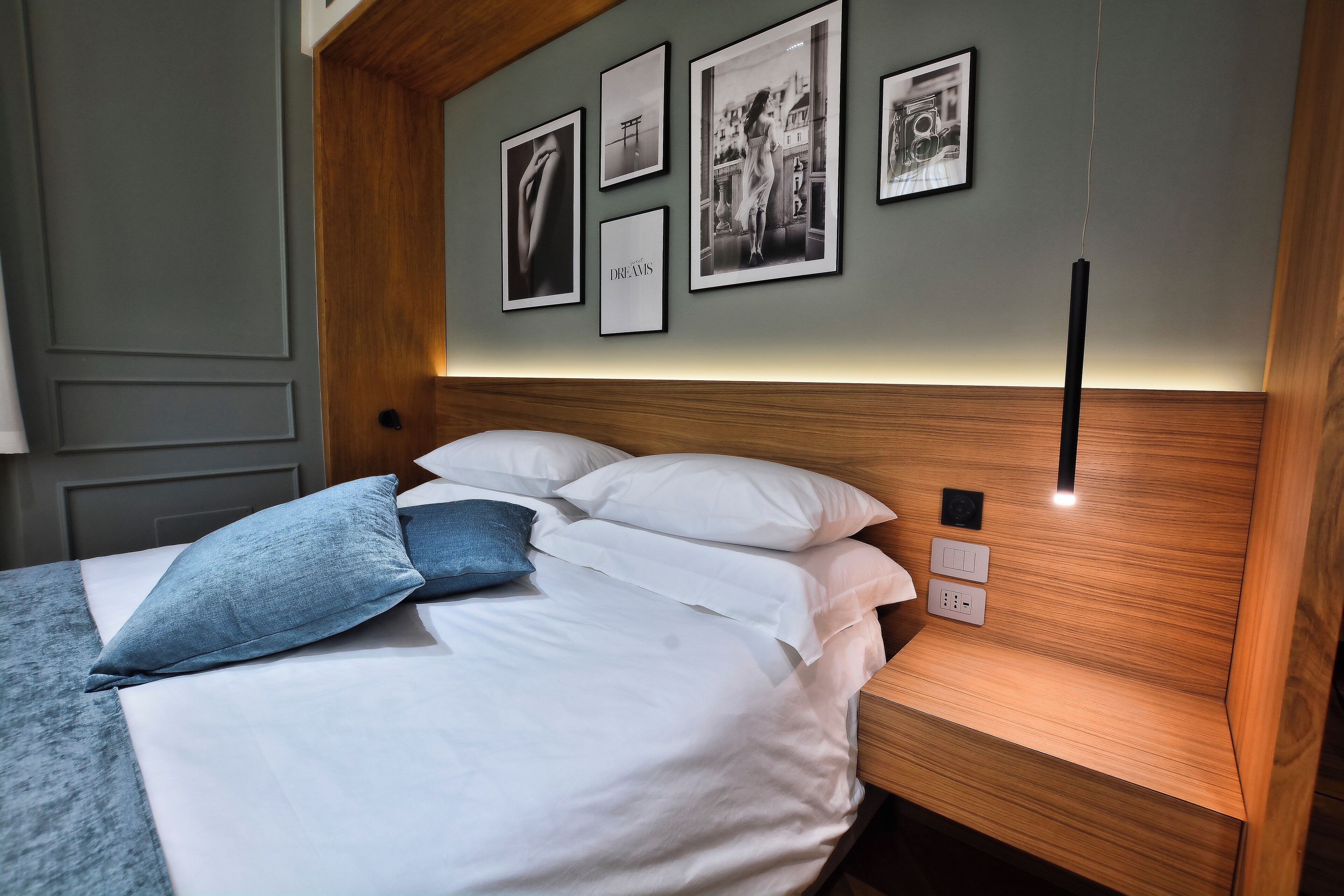 A neatly made bed with white linens and blue pillows, a wooden headboard, and a wall adorned with framed pictures.