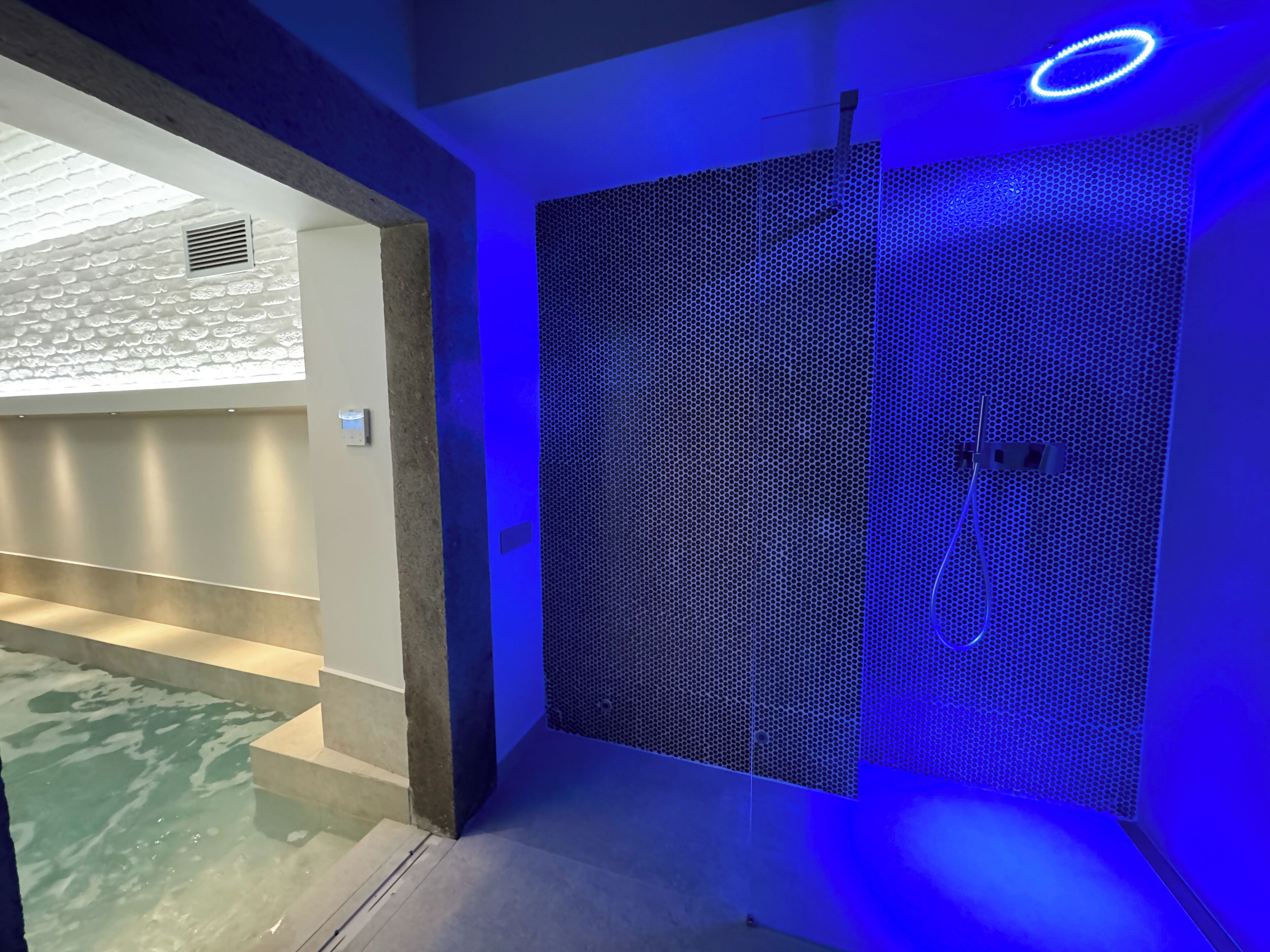 Un baño moderno con zona de ducha que presenta un revestimiento de pared con diseño de panal y iluminación azul.