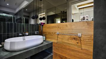 Un baño moderno con un lavabo grande de color blanco, baldosas oscuras y una pared decorativa de madera.