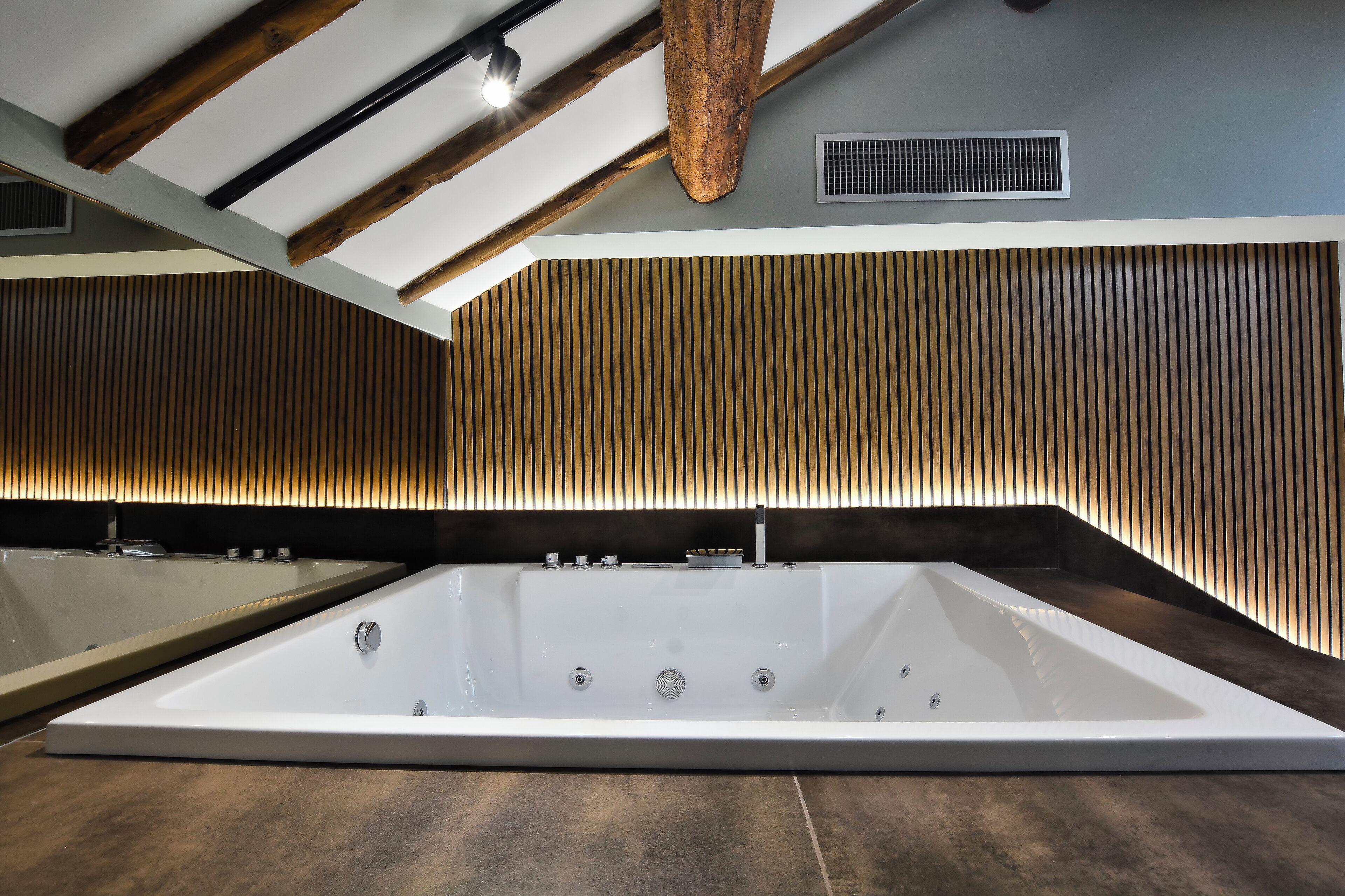 Un baño moderno con una bañera grande de pie, paredes con listones de madera y vigas de madera a la vista.