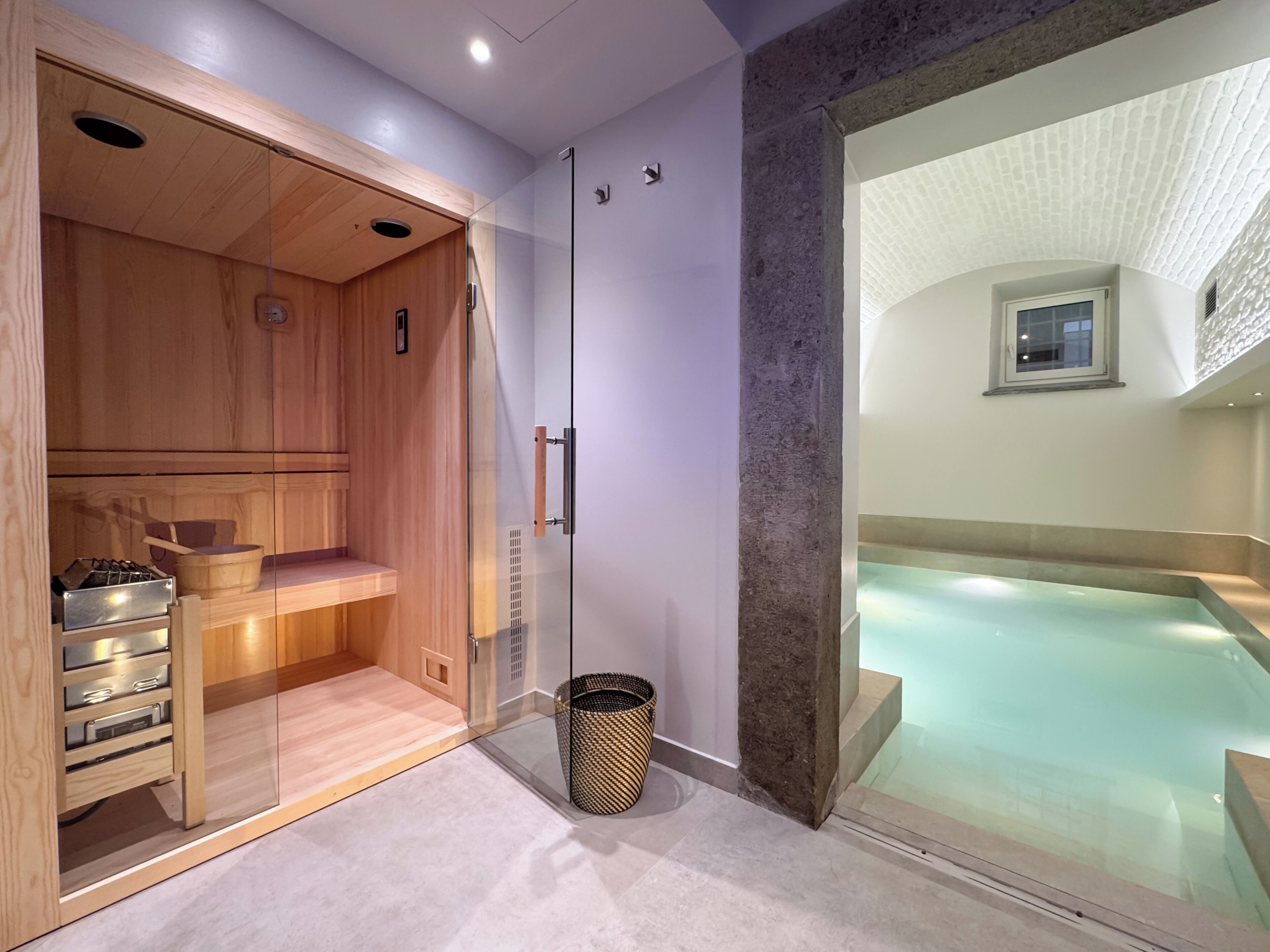 A modern spa room with a wooden sauna, a glass-enclosed hot tub, and a stone pillar.
