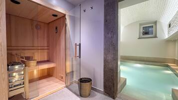 A modern spa room with a wooden sauna, a glass-enclosed hot tub, and a stone pillar.