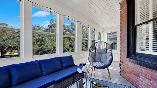 A covered porch with a blue sofa, a wicker chair, and a glass table. - Walkable Home in Thomas Square, Heated Pool Access (Savannah)
