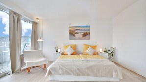 Une chambre moderne avec un grand lit, une chaise, une table de chevet et une fenêtre avec des rideaux.
