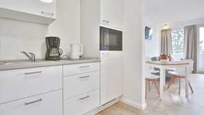 Une cuisine moderne avec des meubles blancs, une machine à café, un four à micro-ondes et un coin repas comprenant une table et des chaises.
