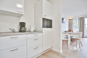 Una cocina moderna con armarios blancos, cafetera, microondas y comedor con mesa y sillas.