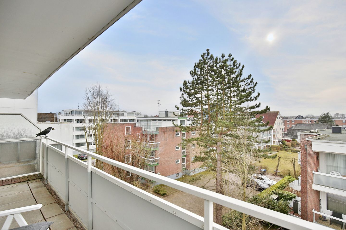 Un balcone con vista su edifici residenziali, un albero e un'auto parcheggiata.