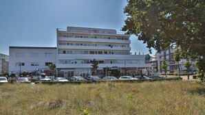 Un immeuble à plusieurs étages, doté d’une façade plate, d’un parking à l’avant et d’un espace verdoyant agrémenté de quelques arbres.