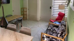 Un espacio habitable compacto con comedor, sofá, televisor y ventana con persianas.