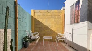 Un patio con suelo de baldosas, sillas de metal blanco, una mesita y una planta de cactus.
