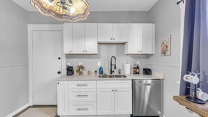 Une cuisine moderne avec des meubles blancs, un lave-vaisselle en acier inoxydable et un luminaire suspendu.