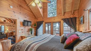 A cozy log cabin room with a large bed, a television, and a desk with a lamp. - Big Blue Ridge | MTN Views, Hot Tub, Pool Table! (Sevierville)