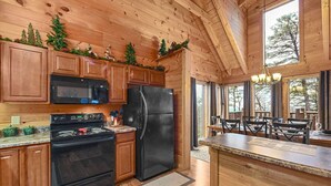A wooden cabin kitchen with a stove, oven, microwave, refrigerator, and a dining area with a table and chairs. - Big Blue Ridge | MTN Views, Hot Tub, Pool Table! (Sevierville)