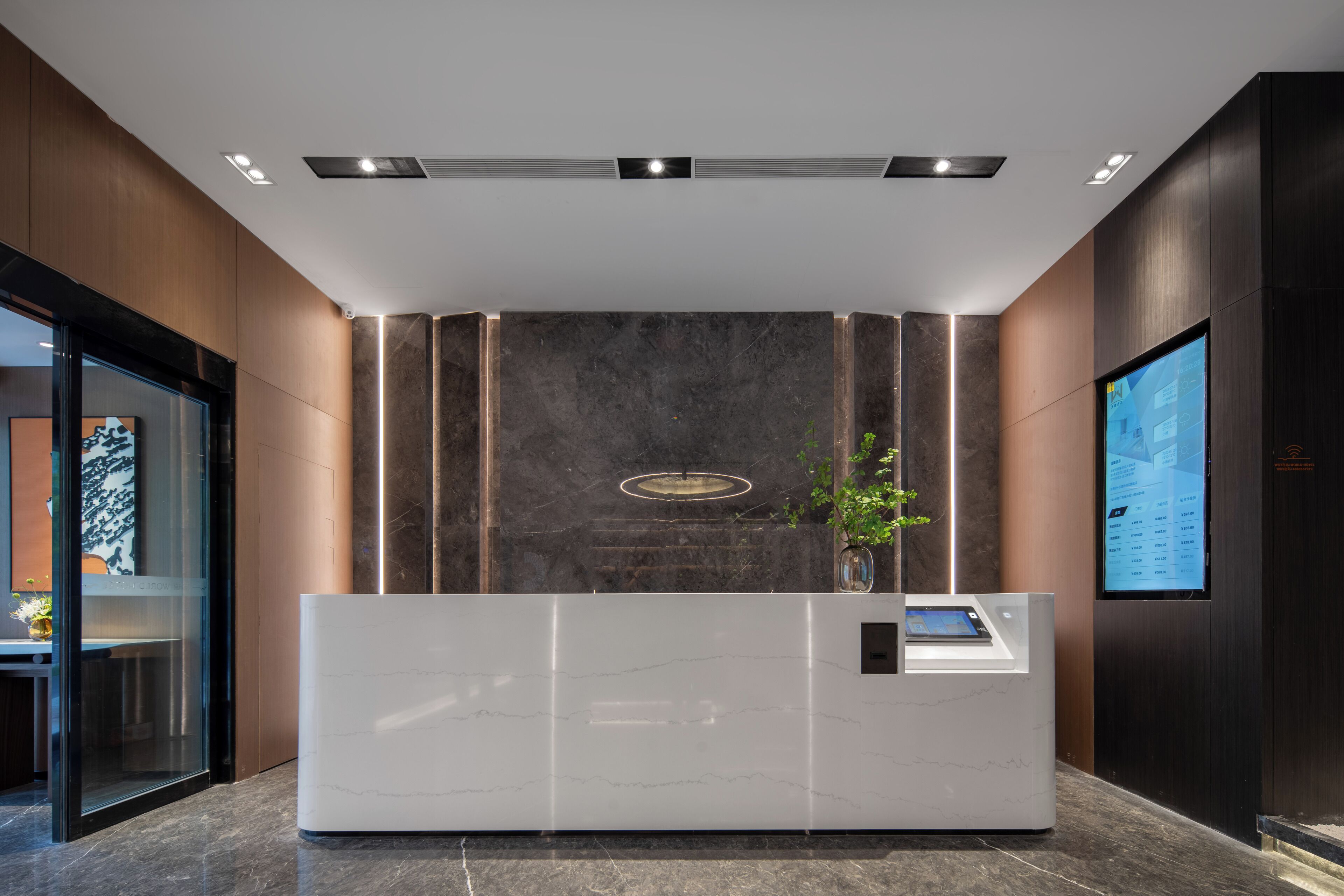 A modern reception desk with a marble top, a digital screen, and a potted plant.