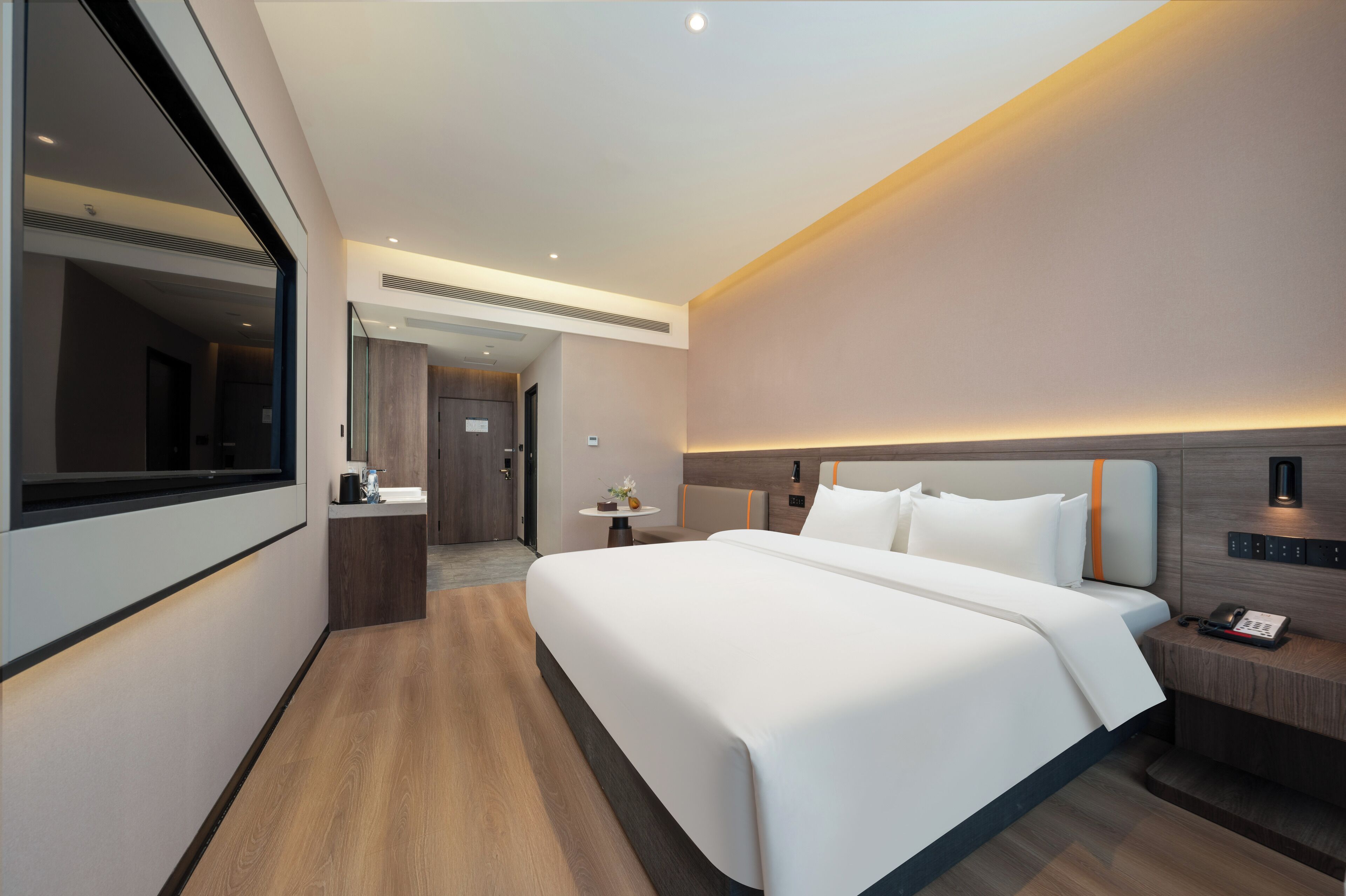 A modern hotel room with a large bed, bedside table, and a small desk with a chair.