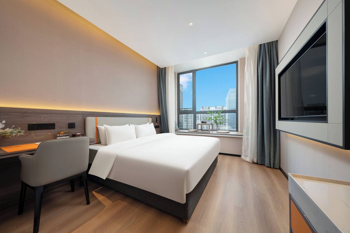 Ein modernes Hotelzimmer mit einem großen Bett, einem Schreibtisch und einem Fernseher.