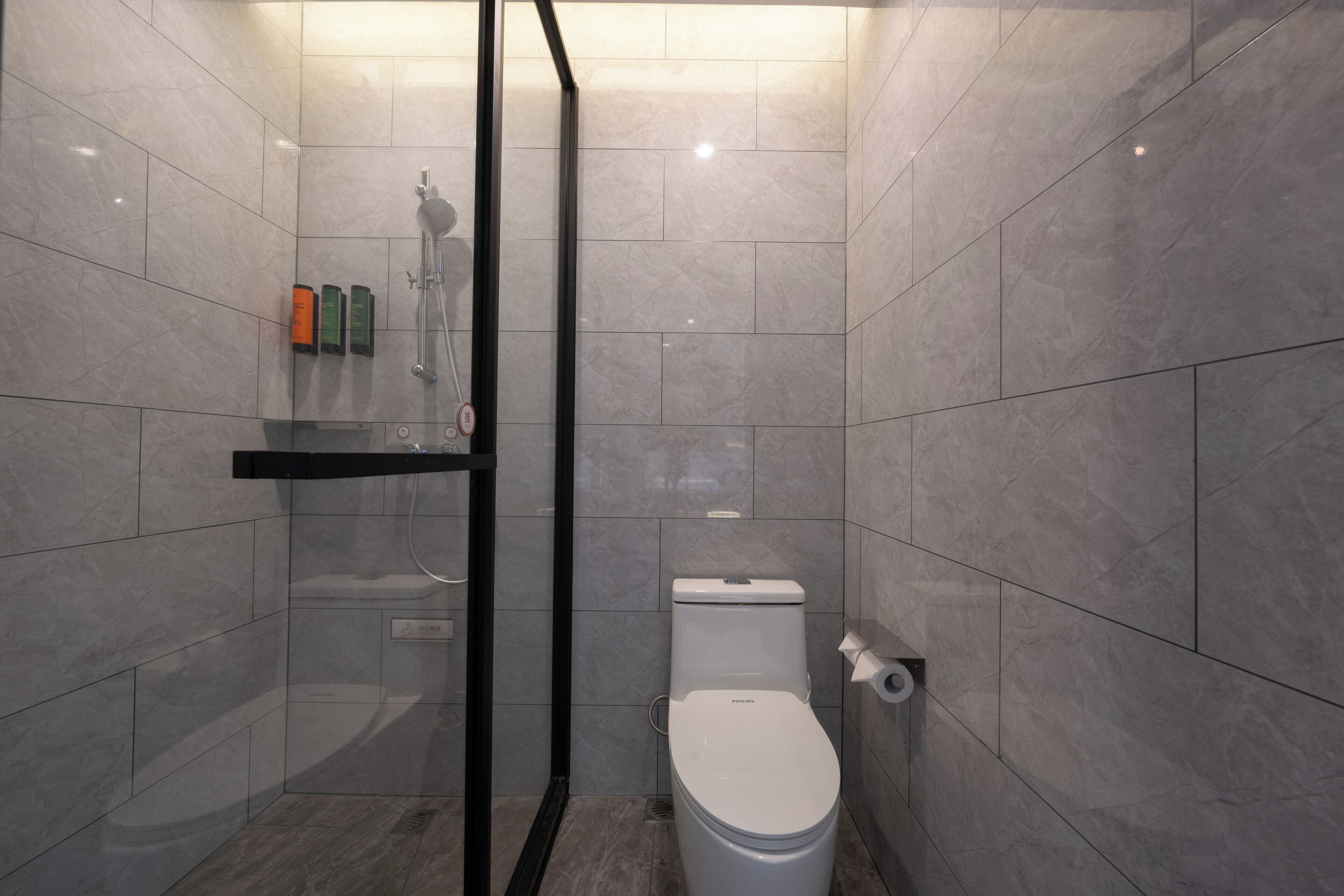 Une salle de bain moderne équipée de toilettes, d’une douche et d’un espace douche clos par des parois de verre.