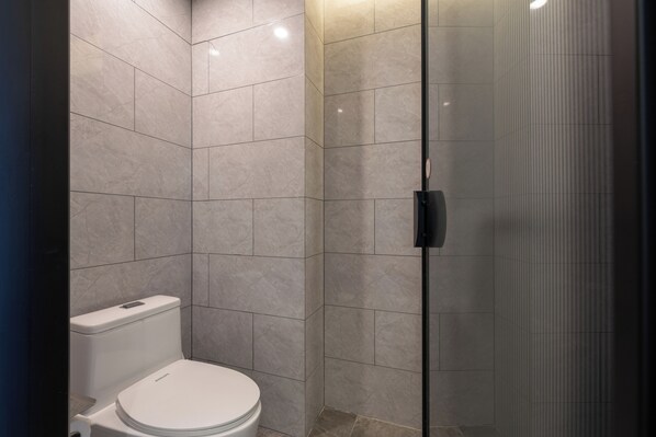 Un baño moderno con inodoro, cabina de ducha de vidrio y paredes de azulejos.