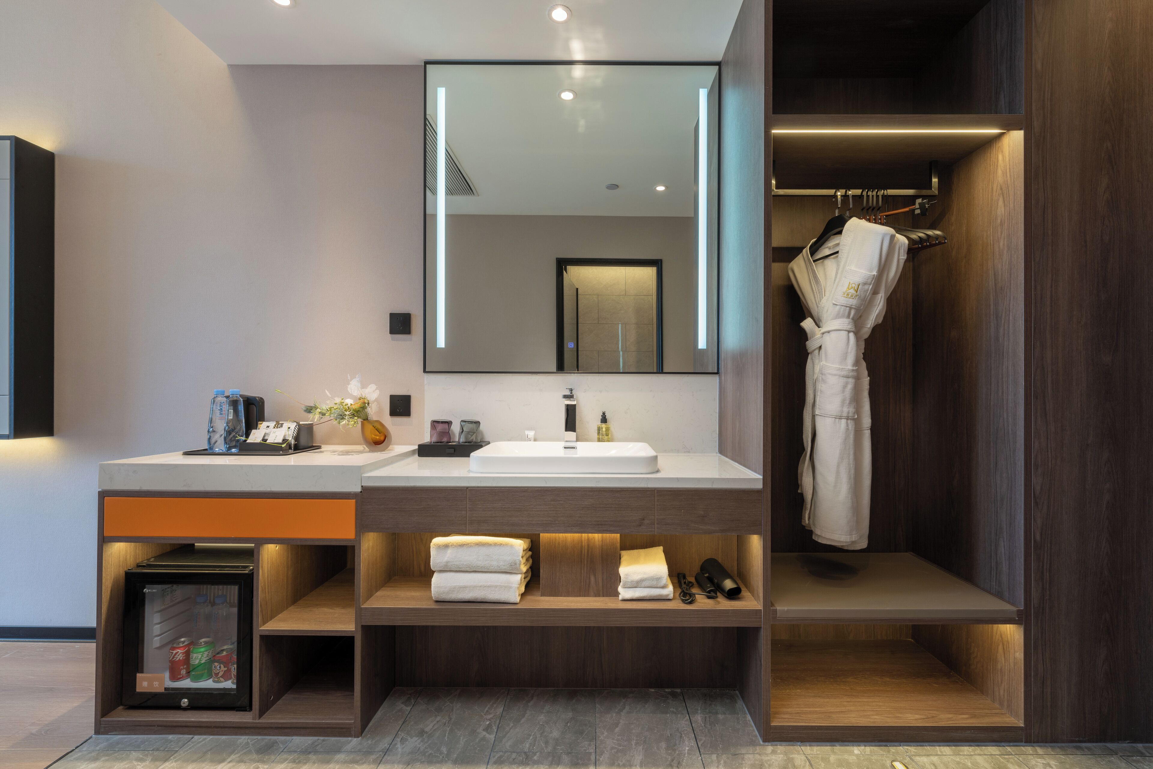 Une salle de bain moderne dotée d’un grand miroir, de deux vasques, d’un porte-peignoir et d’un mini-réfrigérateur encastré.