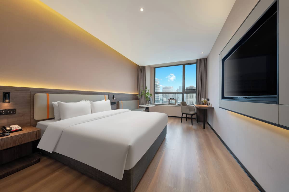 Ein modernes Hotelzimmer mit einem großen Bett, einem Nachttisch, einer Lampe und einem Schreibtisch mit Stuhl.