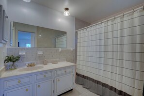 Bathroom features a white vanity with a large mirror and a single faucet, along with a shower area covered by a striped curtain.