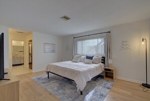 Relax in a serene bedroom with a neatly made bed, bedside table, and large window.