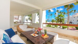 A balcony with a wooden table, white cushions, and a wicker chair.