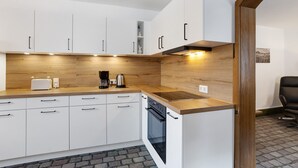 A modern kitchen with white cabinets, a wooden countertop, a built-in oven, and a coffee maker.