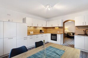 A modern kitchen with white cabinets, a wooden countertop, and a dining area with a table and chairs.