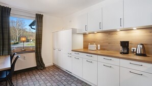 A modern kitchen with white cabinets, a wooden countertop, a coffee maker, and a view of the outdoors.