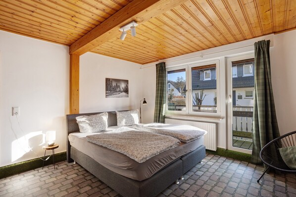 A bedroom with a bed, a bedside lamp, a window with curtains, and a view of the outside.
