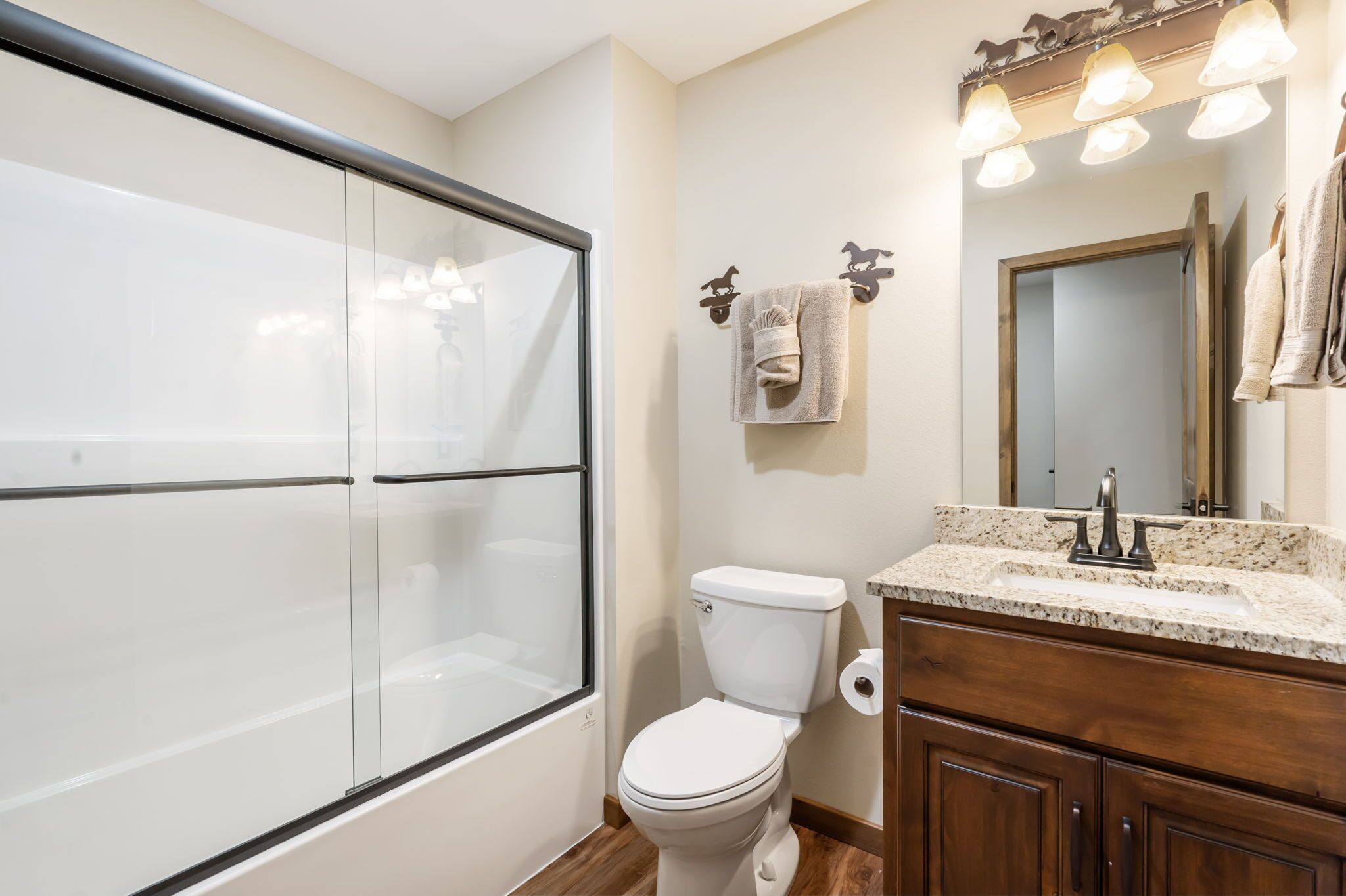 A bathroom with a glass shower enclosure, a toilet, a vanity with a sink, and a mirror with lights.
