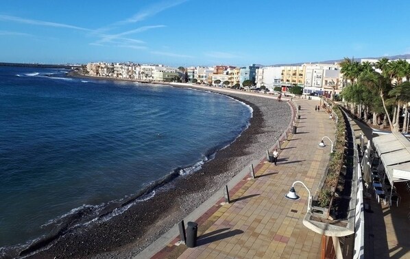 Un paseo marítimo con una playa de guijarros, una hilera de edificios y un cielo despejado.
