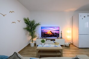 A modern living room with a flat-screen TV, a potted plant, a wooden coffee table, and a white refrigerator.