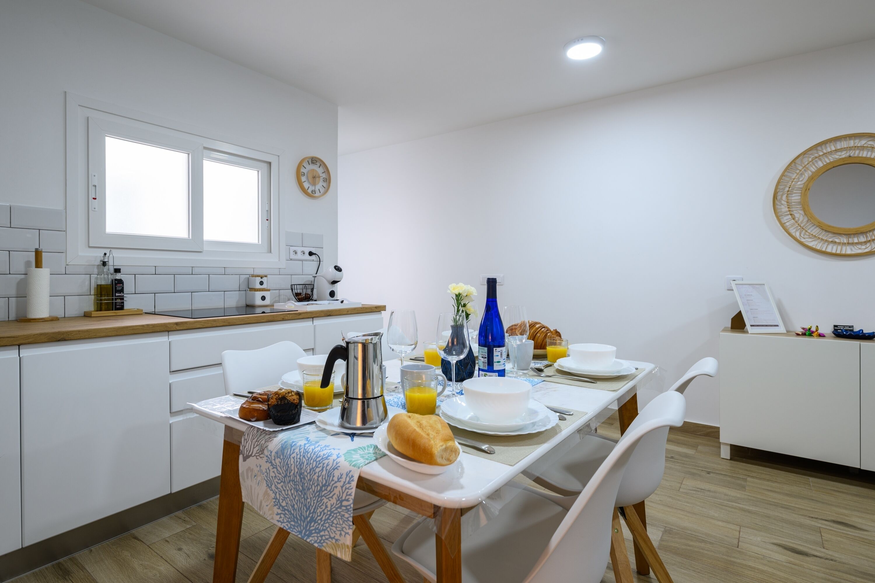 A modern kitchen with white cabinets, a dining table set with breakfast items, and a window above the sink.