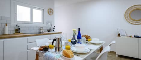 A modern kitchen with white cabinets, a dining table set with breakfast items, and a window above the sink.
