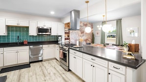 A modern kitchen with white cabinets, stainless steel appliances, a black countertop, and pendant lighting.