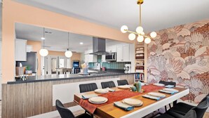 A modern kitchen with a central island, dining area with chairs, and a patterned wall.