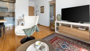 Un salon moderne comprenant un canapé, un téléviseur, une table à manger avec une tasse et une soucoupe, un coin cuisine et un tapis à motifs.