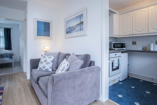 A compact living space with a grey sofa, a small kitchen with white cabinets, and a dining area with a table and chairs.