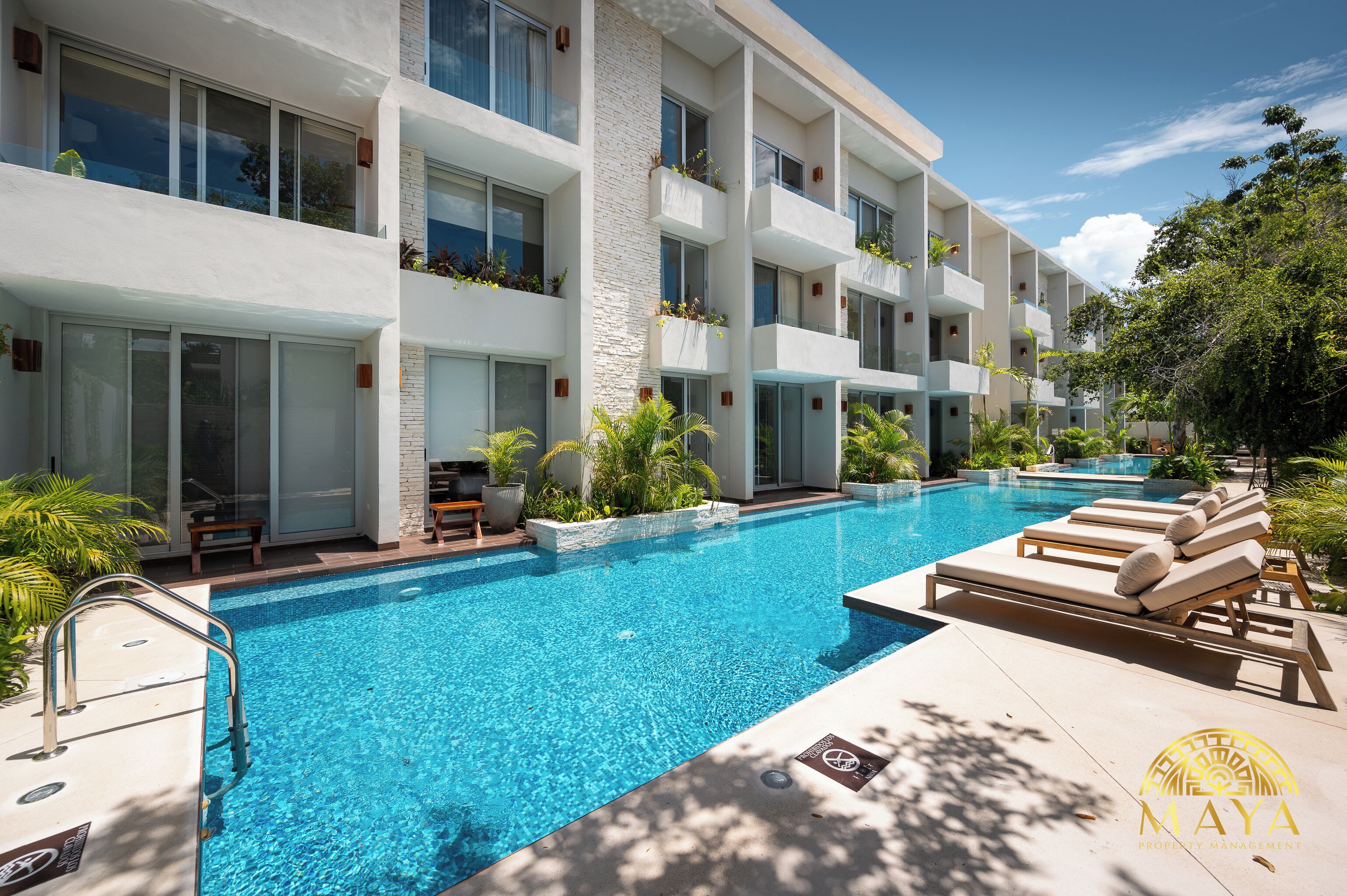 A modern hotel with a swimming pool, outdoor seating, and lush greenery.