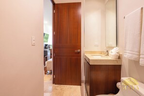 A bathroom with a wooden door, a sink, a mirror, and a towel hanging on the wall. - NHOA 303B 1BR Condo Pool View Aldea Zama (Tulum)