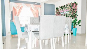 A dining area with a white table, grey upholstered chairs, and a blue accent chair. A decorative wall with greenery and a neon sign is visible. - House Hotel in San Andres Island (San Andrés)