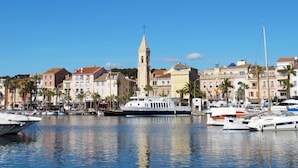 Ein Yachthafen mit vertäuten Booten, einem markanten Turm und Gebäuden mit Balkonen und Palmen.