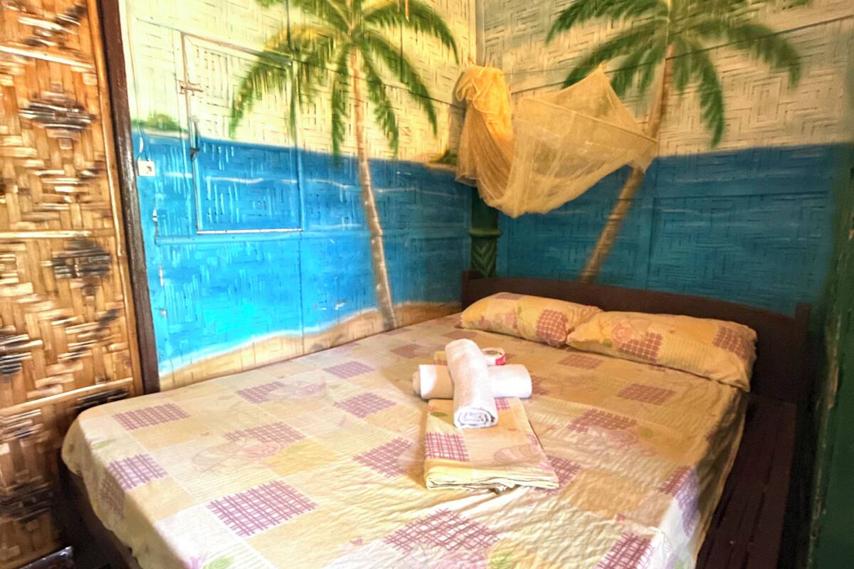 Una habitación con una cama, una puerta de madera y un mural de palmeras en la pared.
