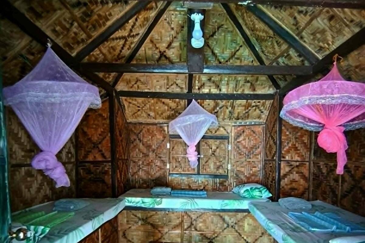Una habitación con dos camas, un banco, mosquiteras y techo de madera.